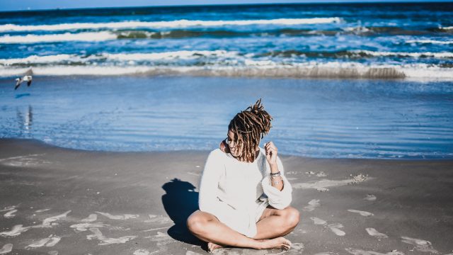 Black Woman Sitting On Sandy Beach By Ocean