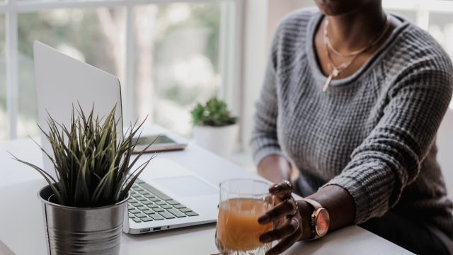 Woman Grabbing Glass of Orange Juice on Desk